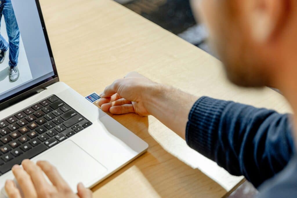 A person using a laptop to insert a memory card while working on digital media content.