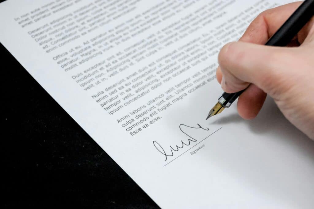 A person's hand holding a pen over a blank sheet of paper with the text "How to Write a Cleaning Proposal Letter" written on it.