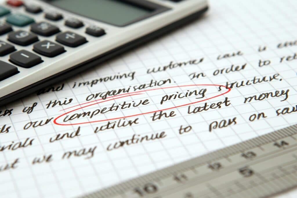 Calculator and handwritten notes on graph paper with the words "competitive pricing" circled in red, representing cost calculation strategies for a cleaning business.