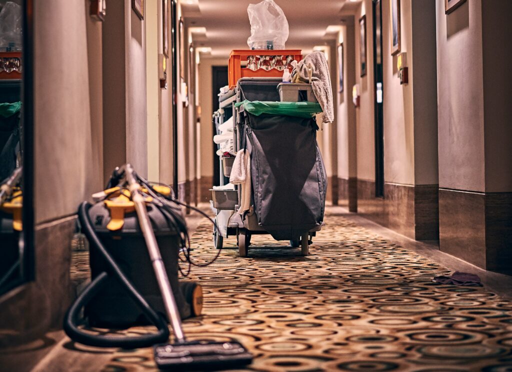 Cleaning cart fully stocked with supplies and a vacuum cleaner parked in hallway.