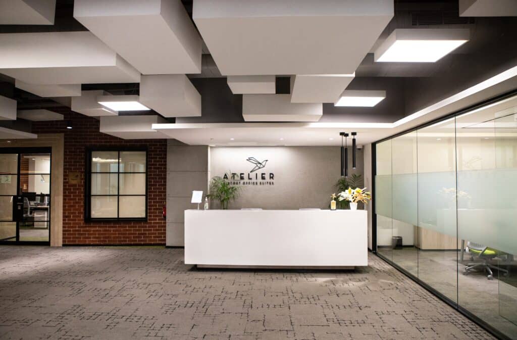 Spacious office lobby featuring a clean reception area with a white desk, modern lighting, and a brick wall, maintained through strict cleaning SOPs.