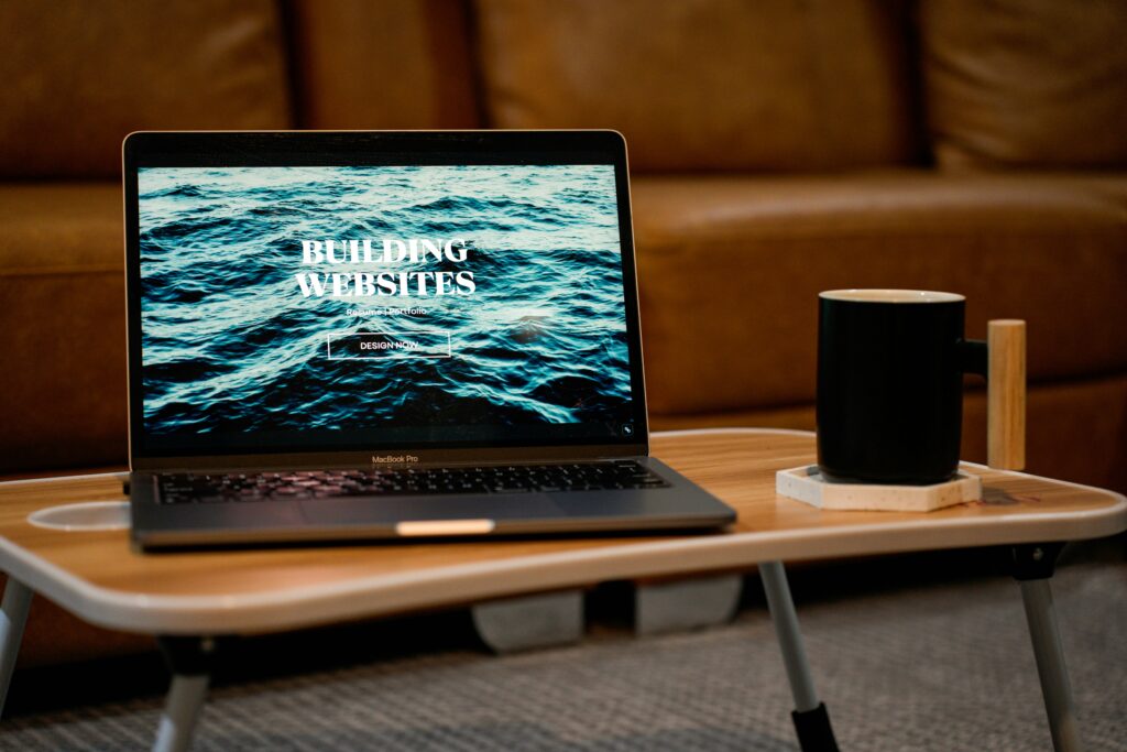 MacBook Pro on a table with a webpage displaying 'Building Websites' and a coffee mug beside it