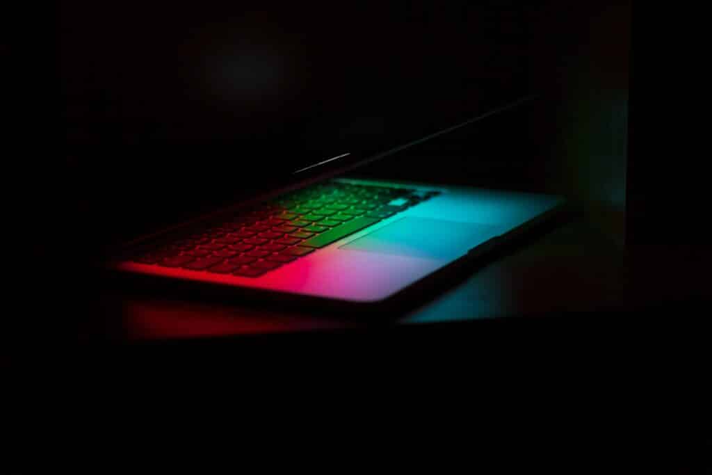 A partially open laptop with a colorful backlit keyboard in a dark room