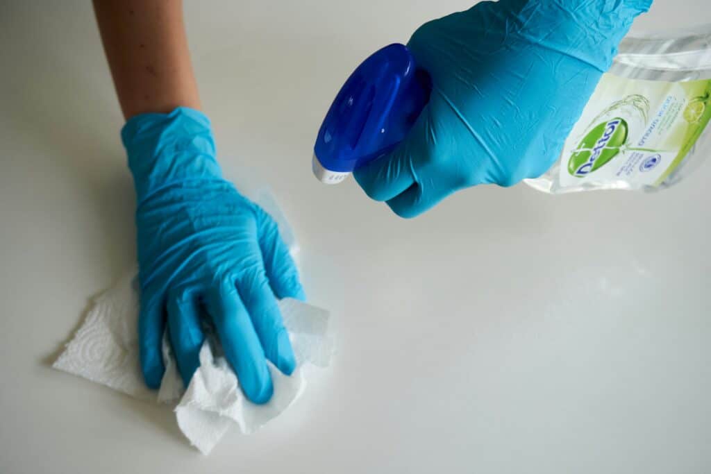 Gloved hands cleaning a surface with spray and paper towel, representing professional cleaning services.