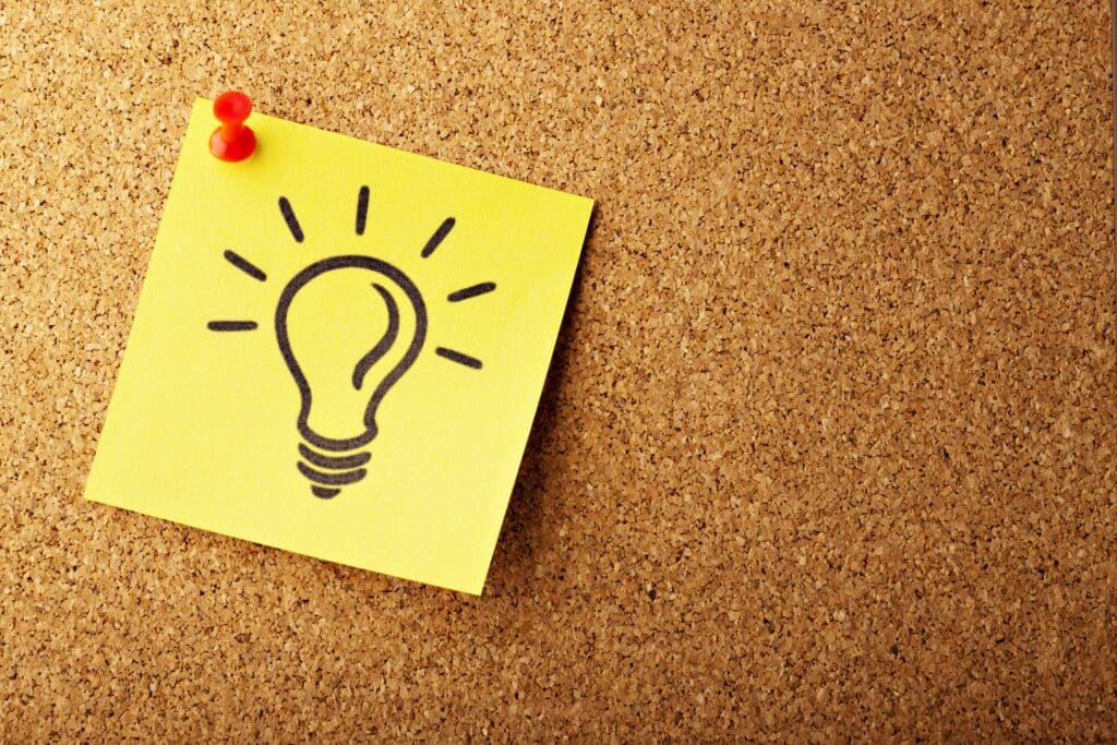 Yellow sticky note with a lightbulb drawing pinned on a corkboard, representing a creative idea for starting a cleaning business.