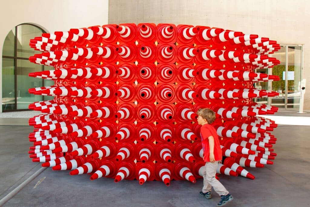 A young child exploring an art installation made of stacked red and white traffic cones arranged in a geometric pattern used as a metaphor for seo keywords for cleaning business