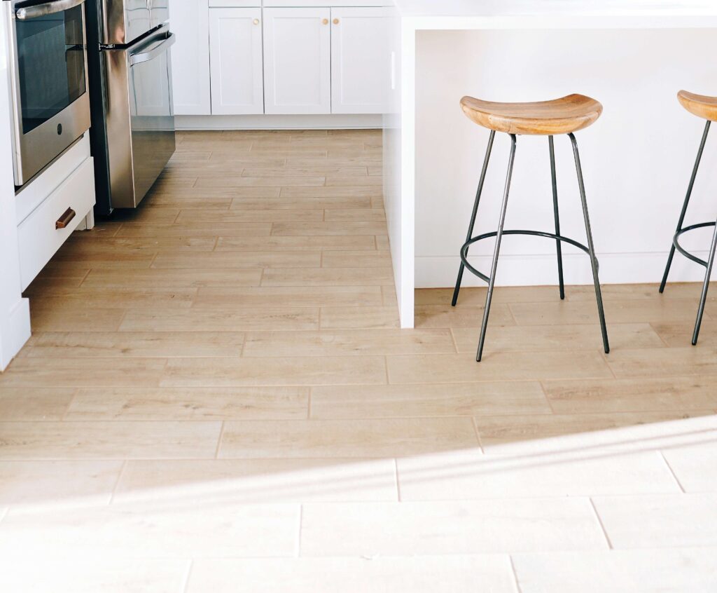 Sleek kitchen with light wood tile flooring and barstools under a white countertop.