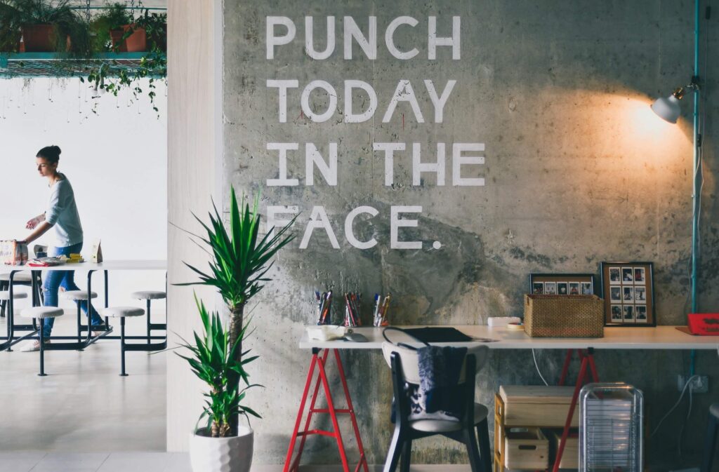 Modern workspace with the words "Punch Today in the Face" on a clean concrete wall, emphasizing the importance of maintaining professional environments.