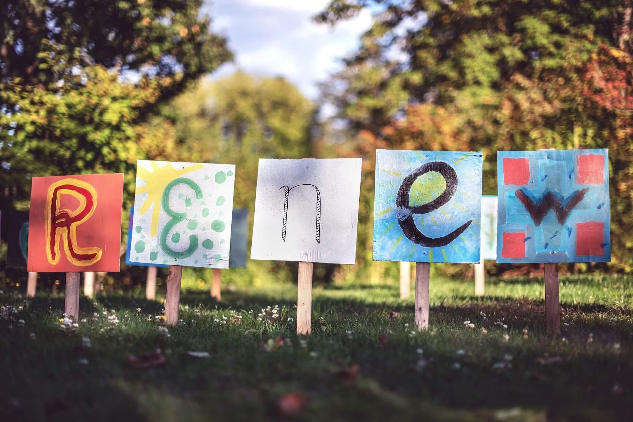 Colorful handmade yard signs spelling “renew” displayed on grass in a sunny neighborhood—ideal for promoting local cleaning services with curb appeal.