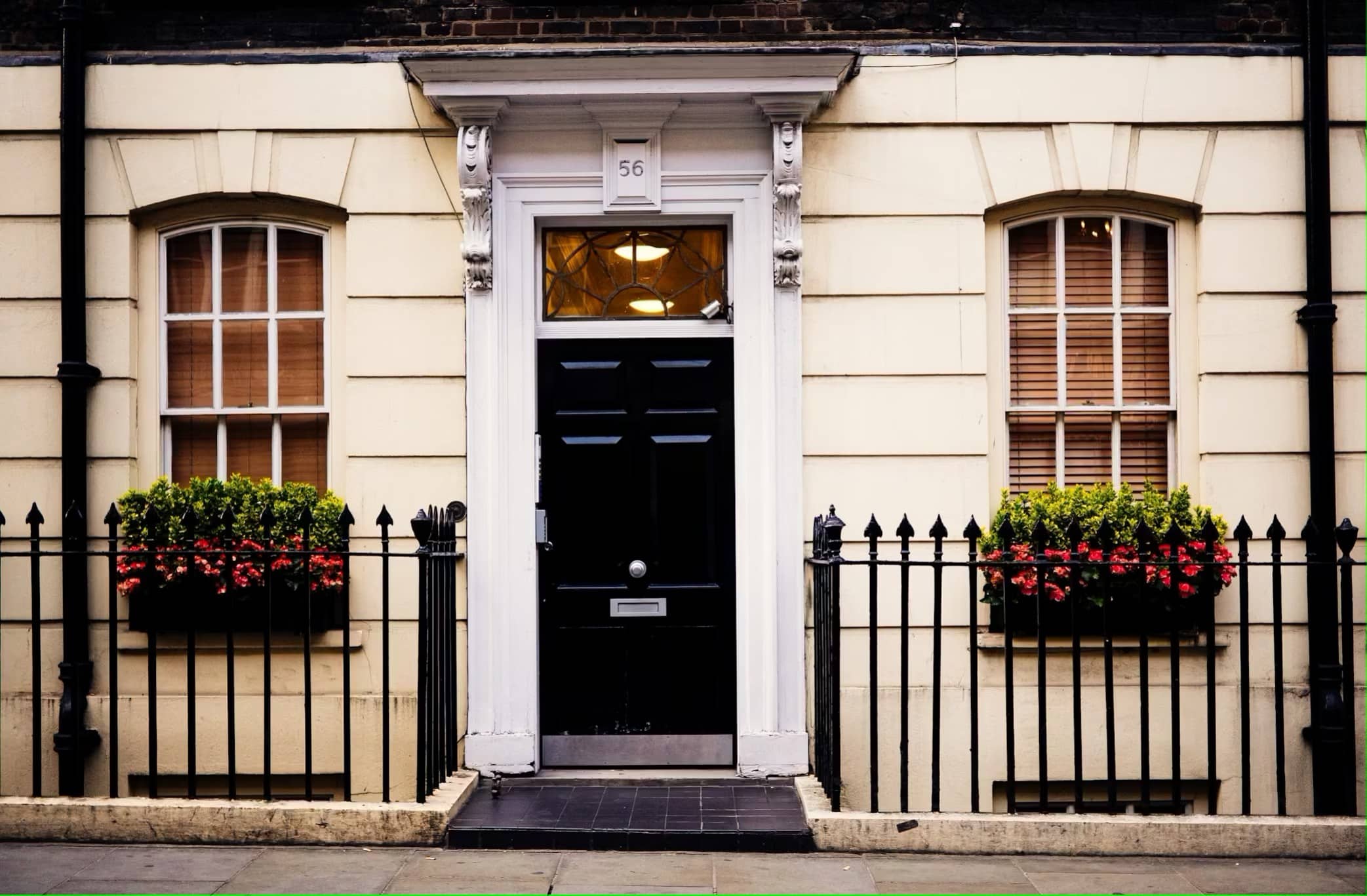 Elegant black front door of a townhouse with flower boxes and wrought iron fence, ideal location for door hanger marketing campaigns.